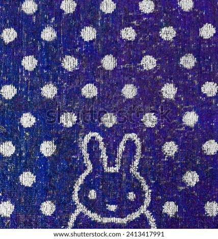 The image captures a towel texture with a bunny and white snowflakes on a blue background. The composition evokes a cozy winter atmosphere, highlighting delicate details and subtle chromatic contrast