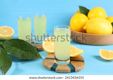 Tasty limoncello liqueur, lemons and green leaves on light blue table