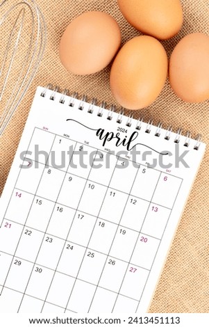 April 2024 Desk calendar and fresh eggs with egg whisk on burlap background.