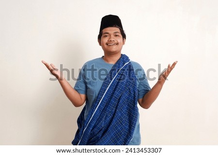 Wow amazed young asian muslim boy wearing cap and scabbard standing with open palm hands. Isolated on white Royalty-Free Stock Photo #2413453307