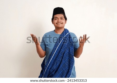 Smiling young asian muslim boy wearing scabbard and cap standing with praying hand gesture. Isolated on white Royalty-Free Stock Photo #2413453313