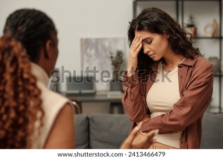 Offended and upset brunette girl touching forehead while standing in front of her irritated girlfriend making accuses during quarrel Royalty-Free Stock Photo #2413466479