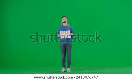 A woman with her mouth taped with black tape holds a poster with the inscription Free speech. Protestant woman fighting for her rights on a green screen.