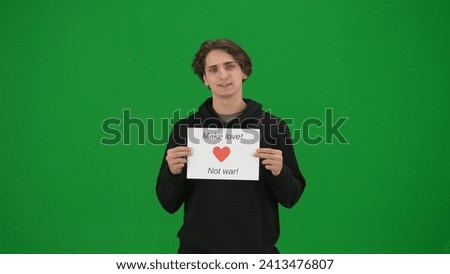 Young man holding a placard that reads Make love no war. Man activist in studio on green screen close up. Anti war slogan, calling for peace. Chroma key.