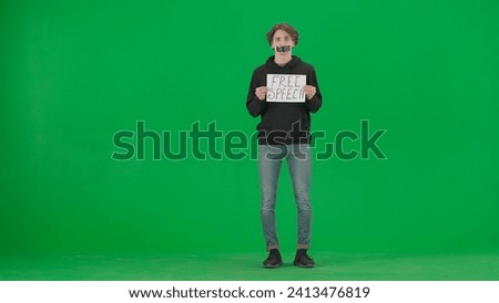A man with his mouth taped with black tape holds a poster with the inscription Free speech. A Protestant man with a placard in the studio on the green screen.