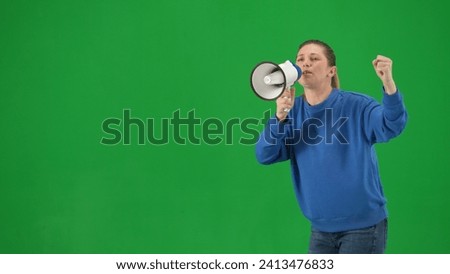 Female activist with raised fist shouting into megaphone in studio on green screen. Front view of a pro protest woman walking close up. Protest action, fight for women's rights, strike.