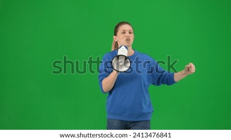 Female activist with raised fist shouting into megaphone in studio on green screen. Front view of a pro protest woman walking close up. Protest action, fight for women's rights, strike.