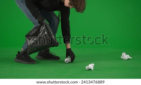 A male volunteer wearing black gloves and carrying a trash bag picks up trash on the green screen close up. Voluntary free work assistance help concept.