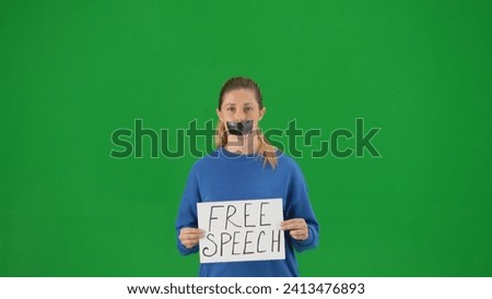 A woman with her mouth taped with black tape holds a poster with the inscription Free speech, close up. Protestant woman fighting for her rights on a green screen.