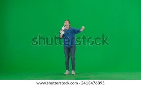 Female activist with raised fist speaking menacingly into megaphone in studio on green screen. Protest action, fight for women's rights, strike. Advertising, promo, chroma key.