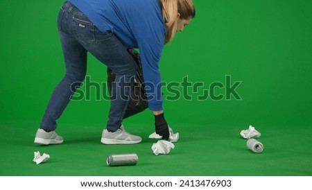 A female volunteer wearing black gloves and carrying a trash bag picks up trash on the green screen close up. Voluntary free work assistance help concept.
