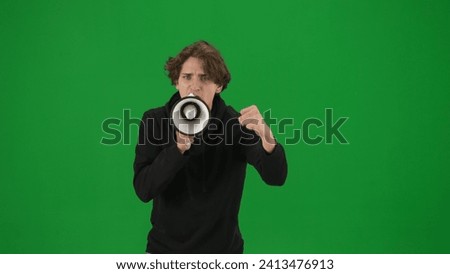 Male activist with raised fist shouting menacingly into megaphone in studio on green screen. Front view of a pro protest man close up. Protest action, fight for human rights, strike.