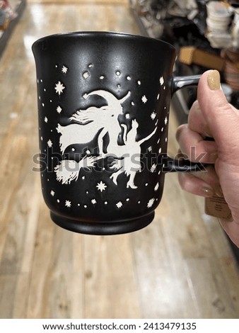 A woman holding up a mug that has a picture of a witch flying on a broom on it.
