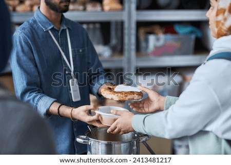 Close up of unrecognizable Middle Eastern man helping refugees at soup kitchen and giving out hot meals Royalty-Free Stock Photo #2413481217