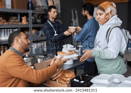 Side view portrait of young Middle Eastern woman wearing headcover receiving free food and donations at refugee help center Royalty-Free Stock Photo #2413481311
