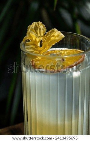 Cocktail with tequila and mezcal, pineapple and lemon juice and sugar syrup. A cocktail in a tall glass is standing on a wooden chair.