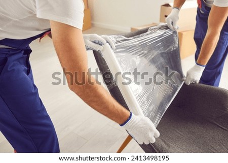 Skilled movers are captured in a close up shot, wrapping an armchair in protective stretch film during home or office moving. This attention to securing of furniture ensures a damage free service. Royalty-Free Stock Photo #2413498195