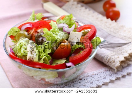 Greek salad in glass dish with fork on napkin and wooden table background