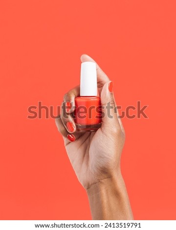Hand holding red nail polish bottle on red background