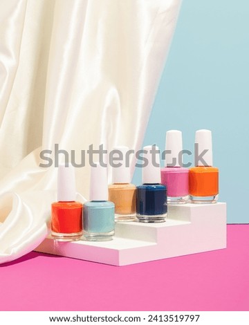 set of colorful nail polishes on stair podium with silky fabric and blue and pink background