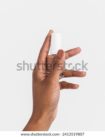 Female hand holding brown nail polish bottle on white background