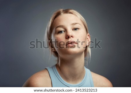 Portrait of a pensive teenage girl. Cute blonde girl in a T-shirt on a dark gray background. Problems during diffcult puberty. Close-up.