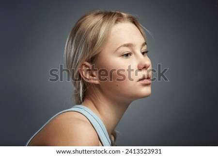 Portrait of a pensive teenage girl. Cute blonde girl in a T-shirt on a dark gray background. Problems during difficult puberty. Close-up.
