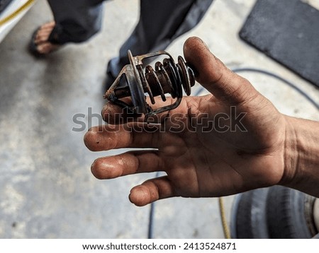 The picture shows a broken car thermostat held in hand by a makanik