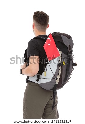 Back view portrait of trekker with a backpack and flag of Turkey isolated on white background. Thirty years old man in black T-shirt posing in studio.