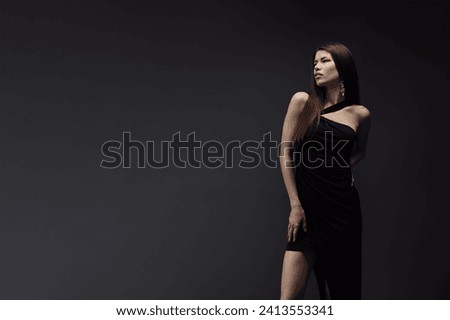 A woman stands confidently in a black dress, striking a pose for a portrait.