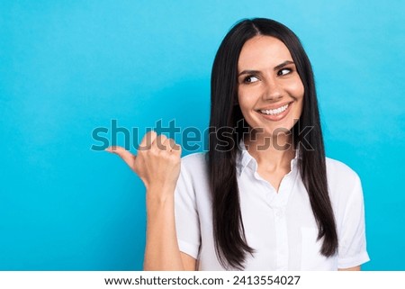 Photo of dreamy shiny girl dressed white shirt looking pointing thumb empty space isolated blue color background