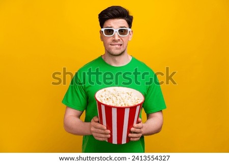 Portrait of nervous guy wear stylish t-shirt in 3d glasses biting lips hold pop corn watch film isolated on yellow color background