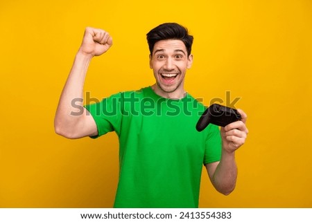 Photo portrait of handsome young brunet guy raise fist play station wear trendy green outfit isolated on yellow color background