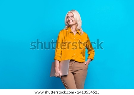 Photo portrait of blonde attractive pensioner woman look empty space wear trendy yellow silky clothes isolated on blue color background