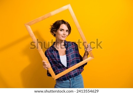 Photo of gorgeous adorable woman with bob hair dressed plaid shirt posing in wood picture frame isolated on yellow color background