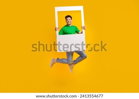 Full length photo of funny good mood pleasant man jumping with frame in hands make instant picture isolated on yellow color background