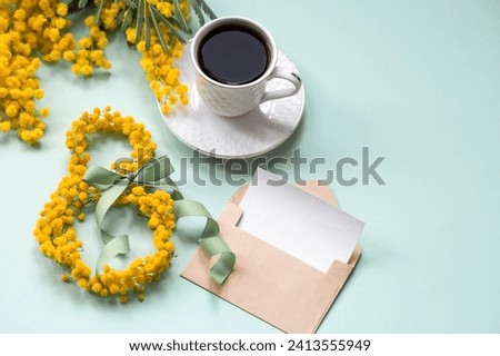 International Women's Day. A banner a beautiful postcard for March 8th. Yellow mimosa flowers in the shape of the number eight, a coffee mug and an envelope with a place for text on a turquoise. Royalty-Free Stock Photo #2413555949