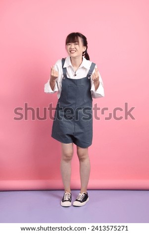 Cheerful lovely young asian woman in overalls casual clothes with gesture of Heart shaped, love, mini heart, cheek heart isolated on pink background. St Valentine's Day, Women's Day, Birthday