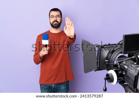 Reporter man holding a microphone and reporting news over isolated purple background making stop gesture Royalty-Free Stock Photo #2413579287