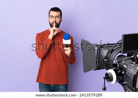 Reporter man holding a microphone and reporting news over isolated purple background showing a sign of silence gesture putting finger in mouth Royalty-Free Stock Photo #2413579289