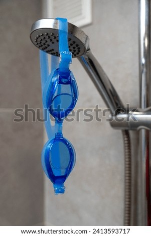 Swimming goggles left hanging in the shower room after a refreshing swim at the pool. The goggles are resting on a hook, with water droplets still visible on them. Royalty-Free Stock Photo #2413593717