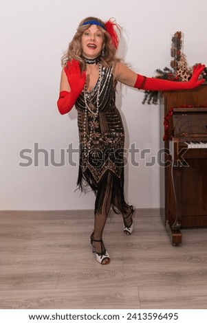 Smiling woman dressed in a flapper costume with red gloves and feathered headband holding out her hands dancing Royalty-Free Stock Photo #2413596495