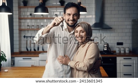 Newly married young couple standing in kitchen smile look at camera husband show bunch of keys from new house. Proud homeowners, rented flat, loan mortgage concept Royalty-Free Stock Photo #2413601345