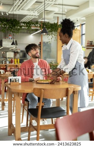 Young dark-skinned waitress putting pizza on a customers table