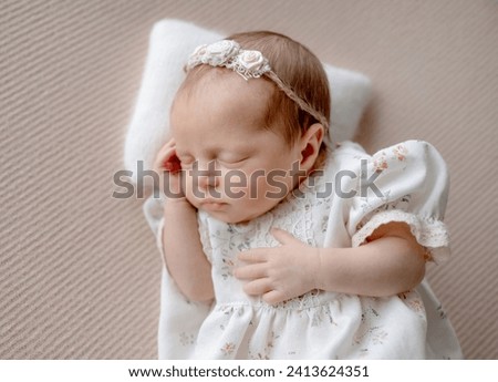 Baby Girl In Dress Sleeps On Beige Fabric Background During Newborn Photo Session In Studio