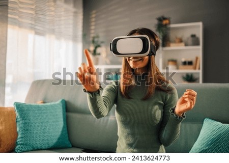 Smile happy woman getting experience while using VR headset glasses of virtual reality at home and gesticulating with hands. Modern technology leisure concept. Royalty-Free Stock Photo #2413624773
