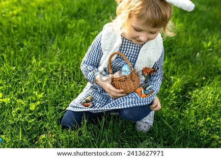 little girl hunts for an egg in a spring garden on Easter day. Traditional outdoor Easter celebration.