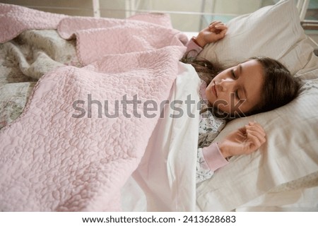 Authentic portrait of Caucasian elementary age, a cute little kid girl seeing sweet dreams while sleeping on the bed with comfortable mattress. Bedtime. Bedchamber furniture. Happy carefree childhood Royalty-Free Stock Photo #2413628683