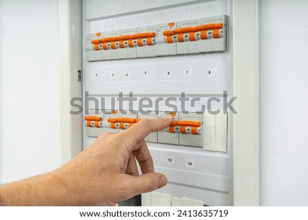 MALE HAND RESETTING TRIPPED CIRCUIT BREAKER IN ELECTRICAL PANEL. FAULT OR BREAKDOWN DUE TO CURRENT OVERLOAD. HOME INSURANCE CONCEPT. Royalty-Free Stock Photo #2413635719