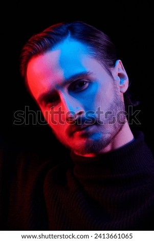 Art photograph in mixed color lighting of a young dark-haired man looking to the camera confidently. Black studio background. Psychological picture.
